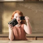 ילדה עומד מחזיקה מצלמה ומצלמת, הילדה עומדת ליד משטח שיש של אבן קיסר מדגם ICON